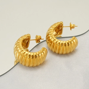 Detail of C-shaped gold hoop earrings with vertical texture on a mirrored surface