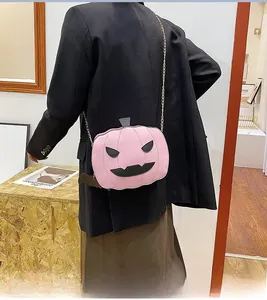 Close-up of pink pumpkin bag with black bat wings and gold chain on a model