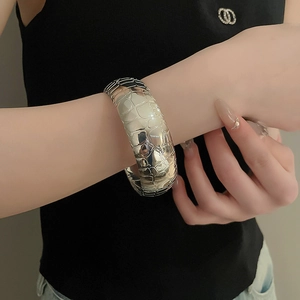 Close-up of a wide silver metal cuff bracelet featuring a textured crocodile skin pattern