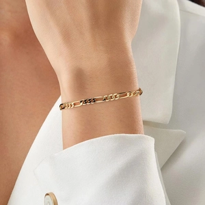 Detailed view of a gold Figaro chain bracelet worn on a wrist with a white blazer