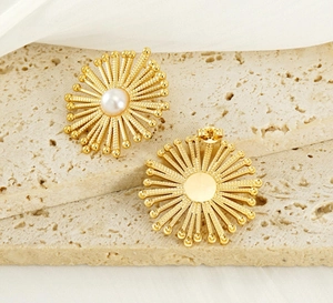 Detailed close-up of gold bohemian flower stud earrings with center pearl on stone surface