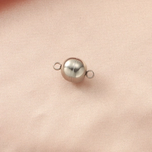Close-up of a spherical silver magnetic clasp for DIY jewelry on pink textured fabric