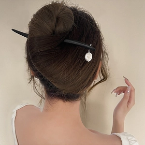 Detail of minimalist flower hair pin with white pearl pendant worn in a sleek bun style