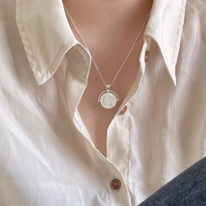 Close-up of a 925 sterling silver coin pendant necklace worn on a beige shirt