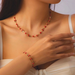 Elegant gold necklace and bracelet set with red cherry beads and green leaf charms