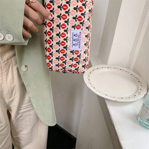 Détail d'une trousse à maquillage en velours côtelé à fleurs tenue par un mannequin