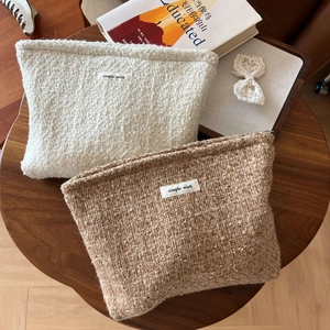 Detail of tweed makeup bags in beige and caramel colors with zip closure on a wooden desk