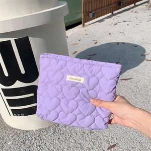 Macro shot of purple quilted heart pattern cosmetic bag held in hand with brand label