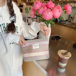 Detail of a large woven striped makeup bag featuring pink accents on a cafe table