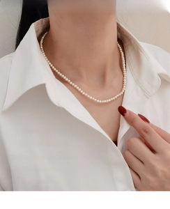 Close-up of a delicate natural pearl necklace worn with a classic white shirt