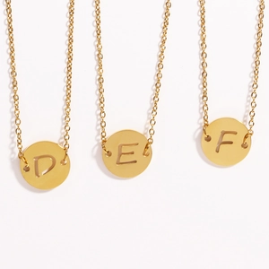 Détail de trois colliers pièces dorées avec lettres évidées D, E et F sur fond blanc