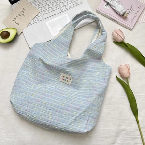 Close-up of the light blue tweed tote bag showing woven texture and brand logo tag