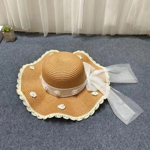 Detailaufnahme vom Strohhut mit weißer Spitze, Blumenakzenten und einer großen Netzschleife