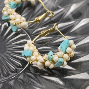 Bohemian gold hoop earrings with white pearls and turquoise stones on a glass plate