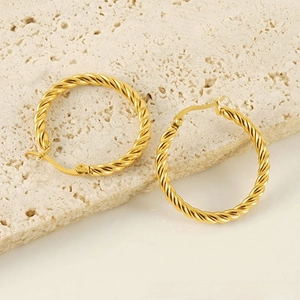 Detailed macro view of gold-plated twisted rope earrings on textured white stone background