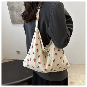 White corduroy tote bag with red strawberry pattern shown on model for size reference