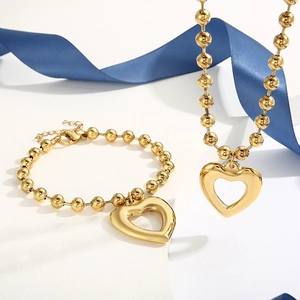 Detailed view of gold beaded necklace and bracelet set with hollow heart pendants
