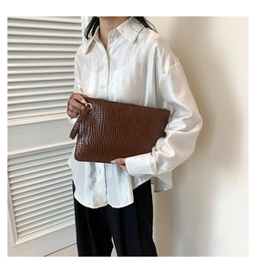 Detail of dark brown crocodile embossed texture envelope clutch bag with gold hardware