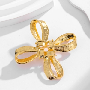 Vintage gold bow brooch with textured metal finish on a minimalist white background