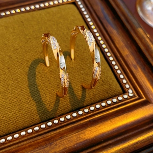 Macro shot of twisted 18K gold-plated C-shaped earrings with zircon on green velvet tray