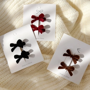 Close-up of velvet bow hair clips in wine red and black on beige knit sweater