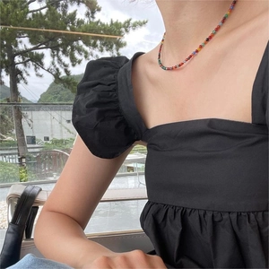 Macro detail of a colorful beaded necklace on a model wearing a black puff sleeve top