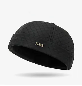 Detail of black quilted docker cap featuring a gold FEWK logo and diamond stitching