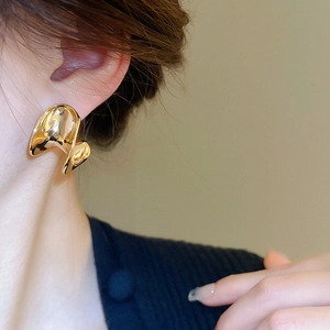 Close-up of minimalist wave-shaped gold-plated C-shaped earrings worn by a model