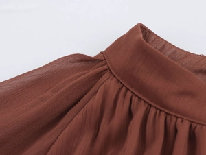 Dettaglio macro dello scollo a balze e del tessuto in chiffon leggero su un abito marrone