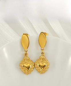 Macro shot of vintage gold heart earrings with embossed radial texture on white porcelain
