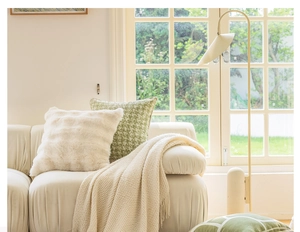 Close-up of fluffy white faux fur pillow with beige knit blanket on a modern sofa