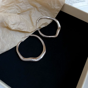 Close-up of irregular silver hoop earrings with organic wave design in a black gift box