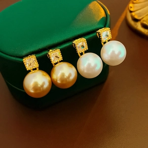 Detail of gold and white pearl earrings with square cubic zirconia studs on jewelry box
