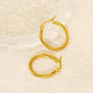 Detail view of gold hoop earrings with twisted texture on a minimalist background