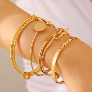 Detailopname van de vijfdelige gouden armbandenset met bedeltjes om een pols