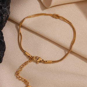 Macro detail of gold-plated double-layer snake chain bracelet with a central knot design