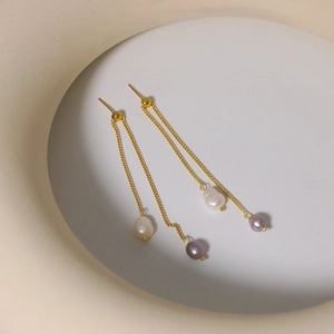 Elegant gold tassel earrings with natural white and purple pearls on a minimalist background