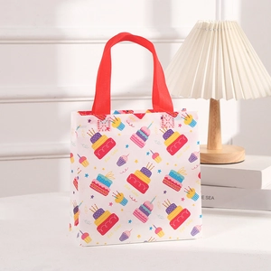 Detail of non-woven birthday gift bag with colorful cake print and red handles