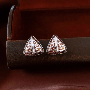 Macro shot of triangle leopard print earrings with metallic edges on a leather jewelry box