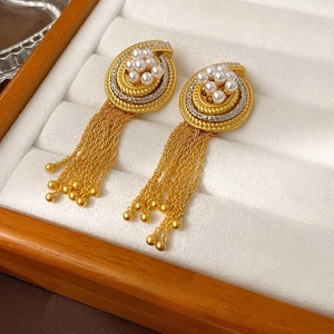 Dettaglio di orecchini vintage dorati con nappa e perle su espositore in velluto bianco