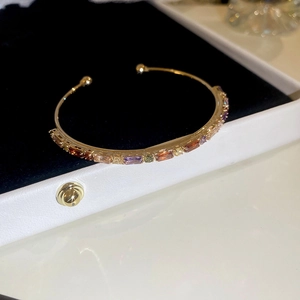 Close-up of golden C-shaped bangle with colorful rectangular gemstones on black velvet