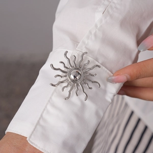 Close-up of silver sunflower cufflinks on a white shirt sleeve showing metallic texture
