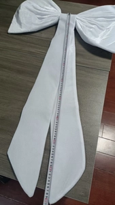 Measurement of large white velvet bow decoration with long ribbon tail on dark wood
