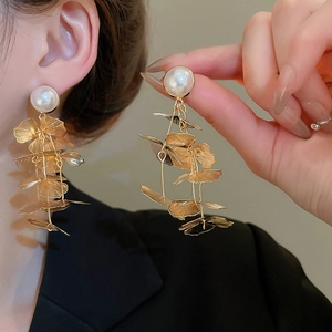 Detail of golden hollow flower tassel earrings with white pearls and metal petals