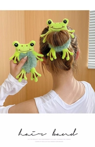 Close-up detail of a cute green frog plush hair tie with big eyes on soft faux fur elastic