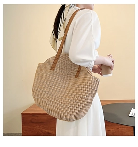 Detail of handwoven straw tote bag with brown leather handles and sturdy cross-stitch seams