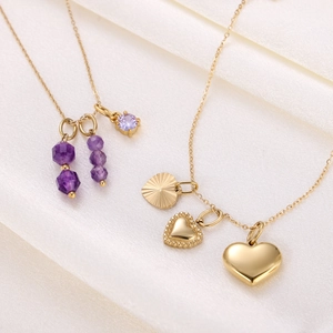 Detail of golden necklaces with purple gemstones and heart pendants on white silk fabric