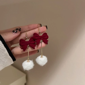 Close-up of red flocked bow earring with a soft white pompom and gold metal links