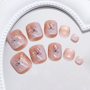 Pink gradient toe nail patches with gold glitter and black bow designs on a tray