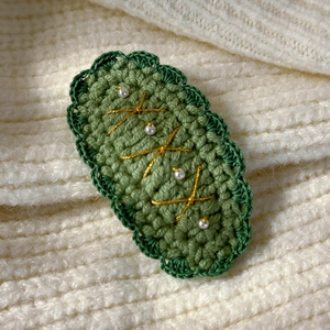 Macro shot of green knitted Christmas tree hair clip with white pearls and gold thread detail